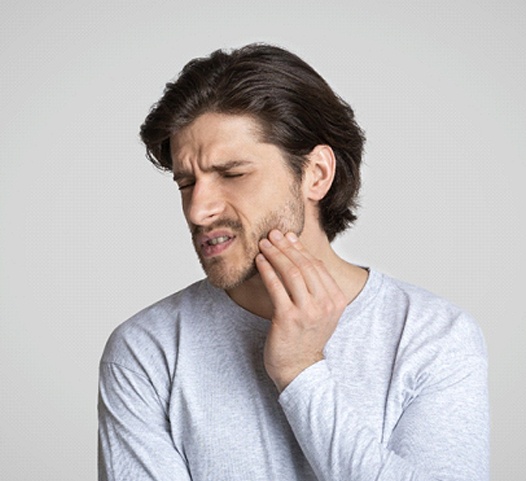 A young male wearing a gray long-sleeved shirt and holding his jaw in immense pain