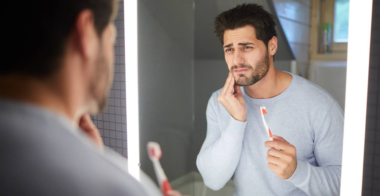 Man in need of periodontal therapy holding cheek while brushing teeth