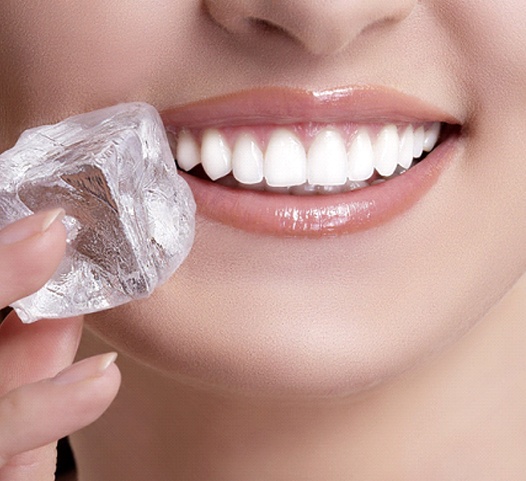An up-close image of a woman holding an ice cube next to her teeth