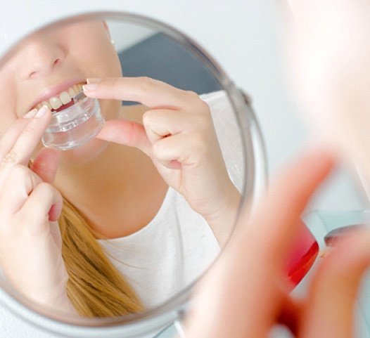 A young girl preparing to insert a mouthguard using a bathroom mirror to help her guide it into her mouth