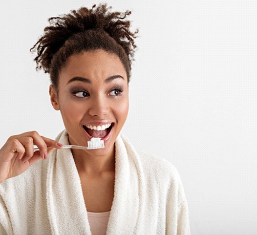 A woman wearing a cream-colored bathrobe and preparing to brush her teeth