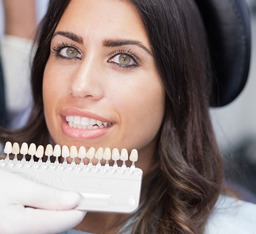 woman smiling while dentist holds up row of veneers 