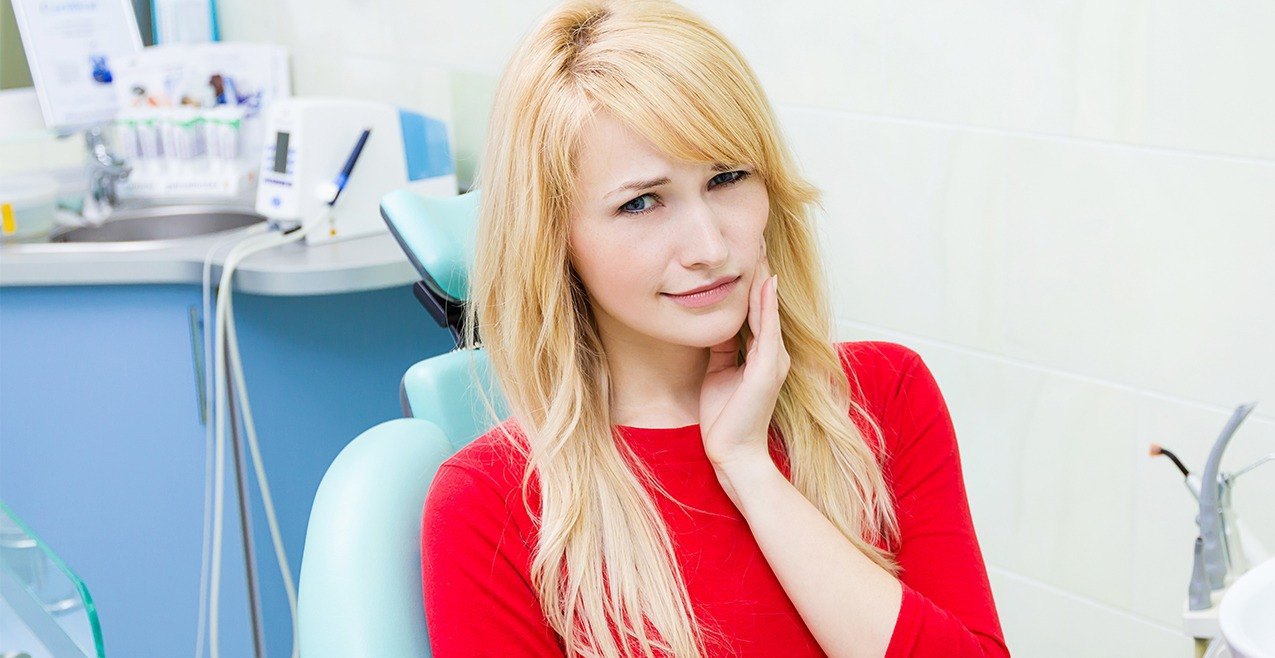 Young woman in dental office for wisdom tooth extraction holding cheek